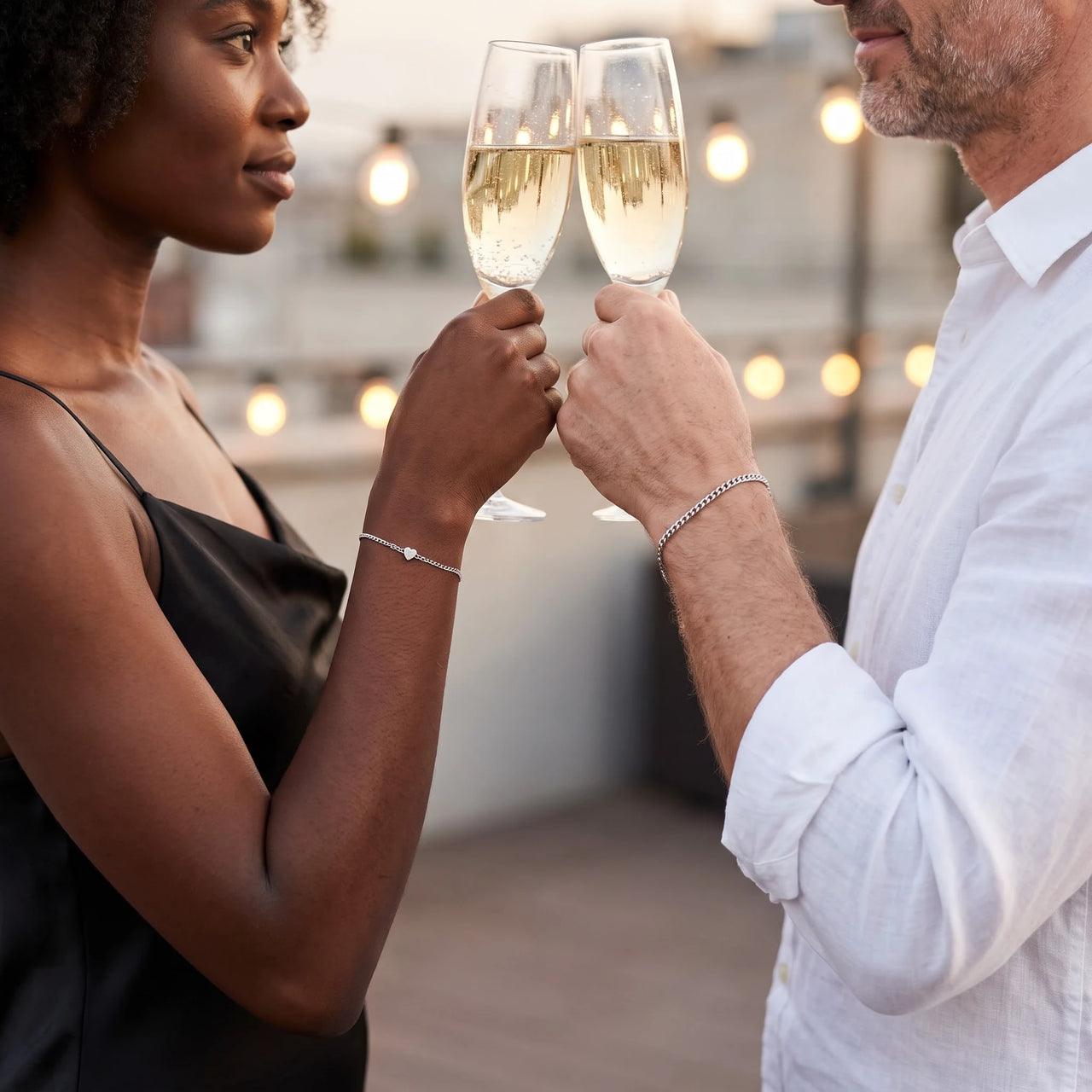 Heart Bond Matching Bracelet Set in Silver — worn by a couple toasting with champagne