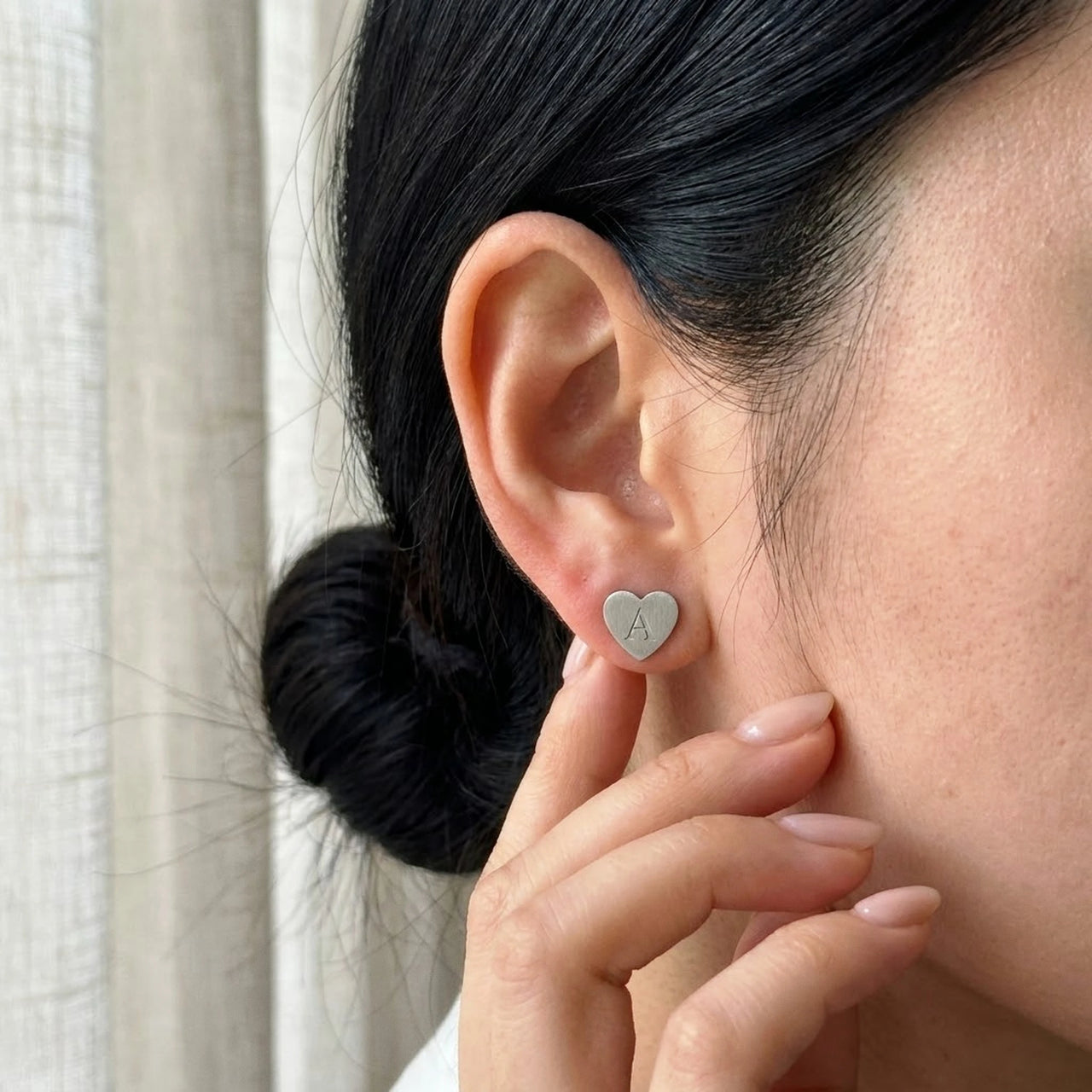 Heart Initial Stud Earrings in Silver held between the fingertips, scale reference | SKU: heart-initial-silver-a
